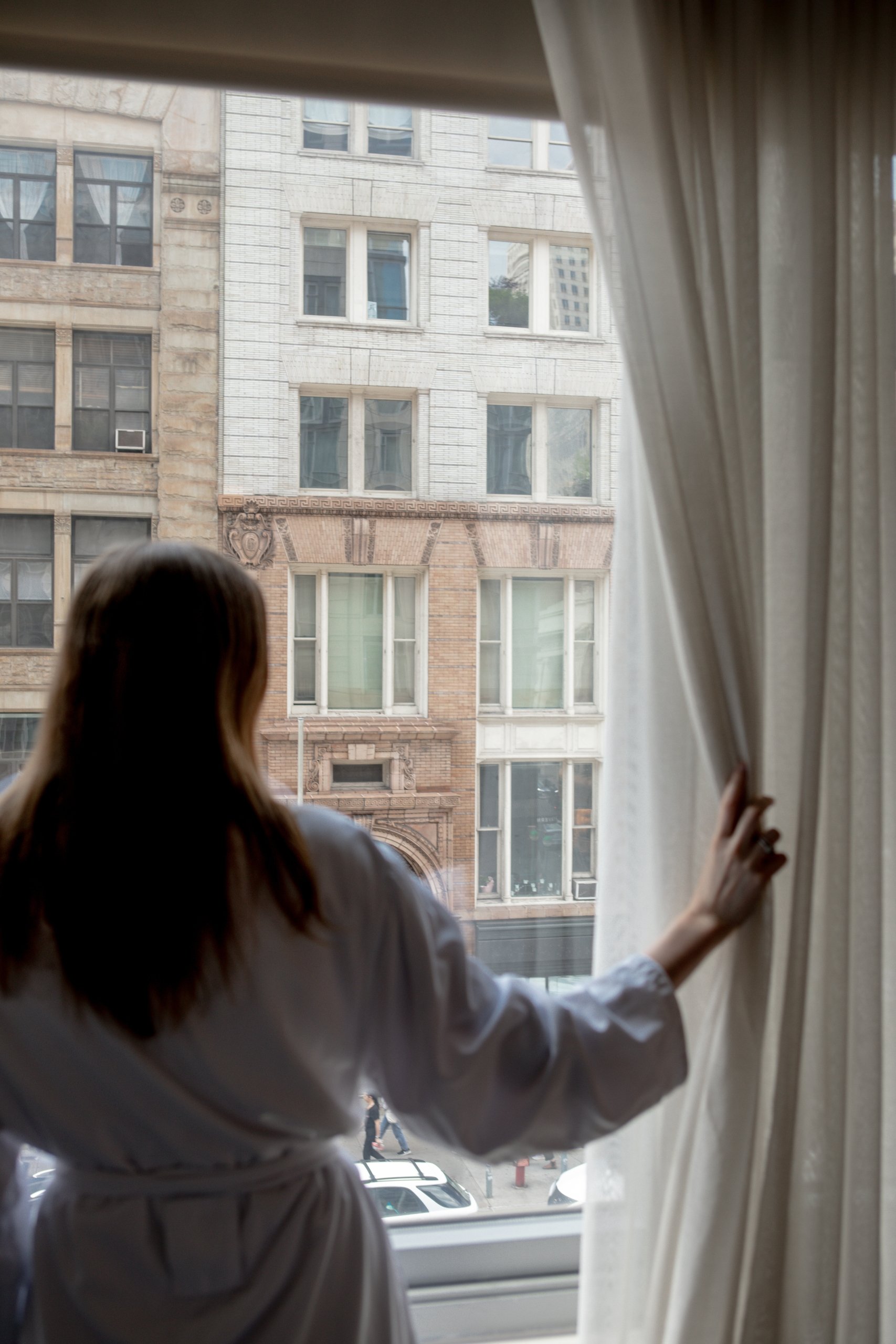 Woman looks through window at lower Manhattan buildings in New York.